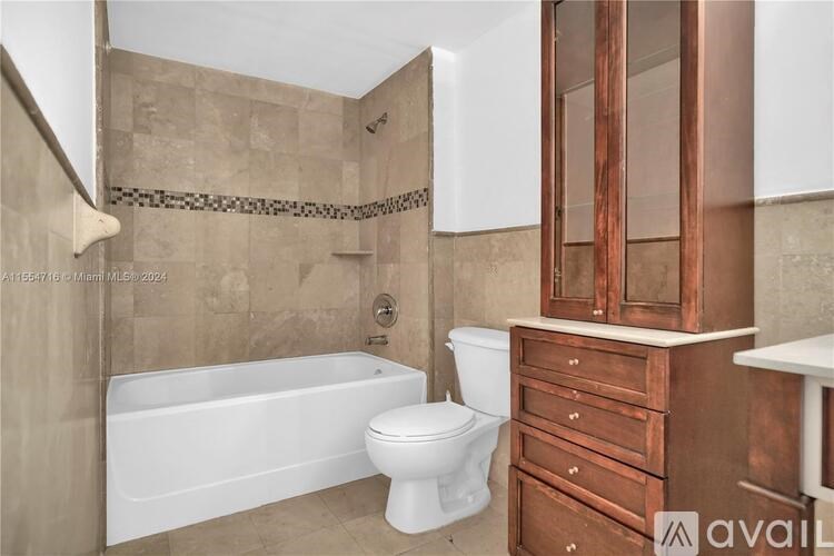 A bathroom with a white tub, toilet, and wooden cabinet.