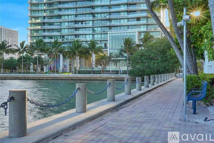 A walkway with a bench and a chain barrier is next to a body of water.