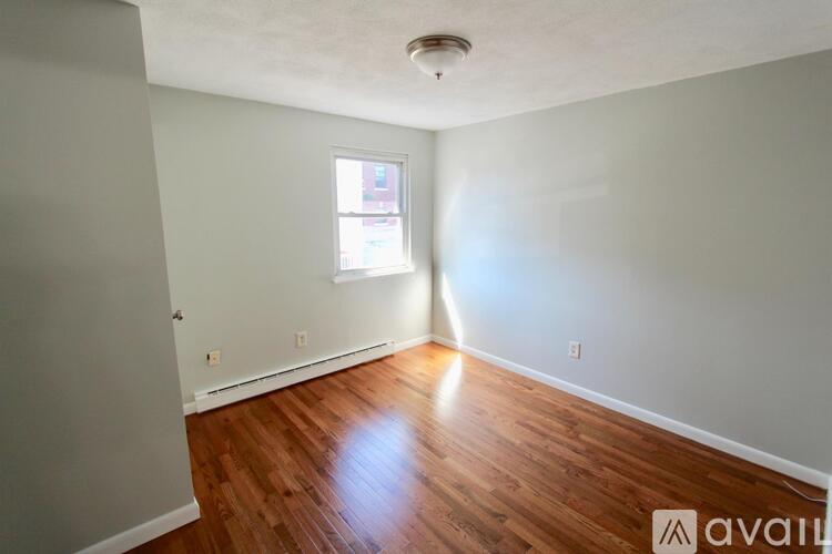 A room with wooden flooring and a window letting in sunlight.