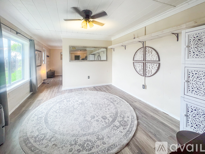 A living room with a rug, a ceiling fan, and a mirror on the wall.