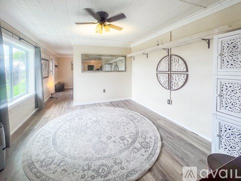 A living room with a rug, a ceiling fan, and a mirror on the wall.