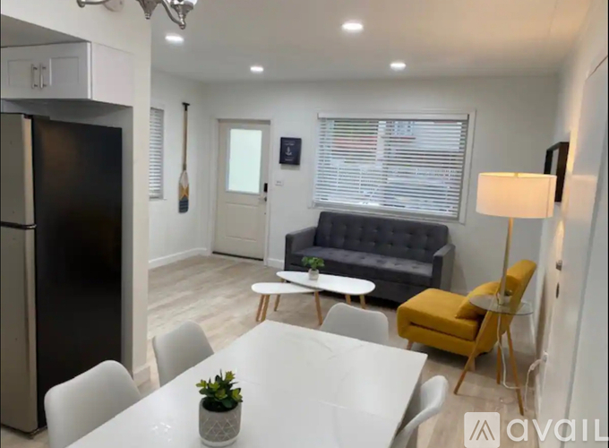 A modern kitchen with a black fridge, white dining table, and a grey sofa.