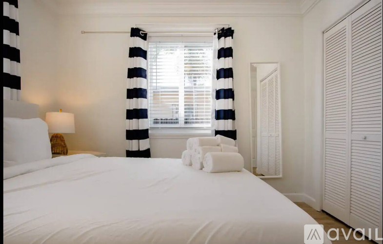 A bedroom with a large bed and a window with striped curtains.