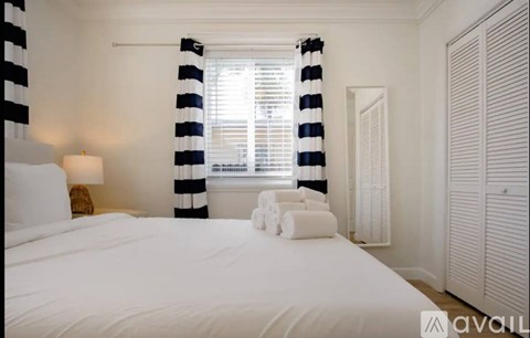 A bedroom with a large bed and a window with striped curtains.