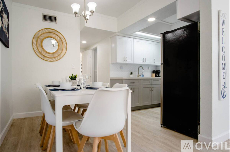 A white dining table with four chairs and a framed mirror on the wall.