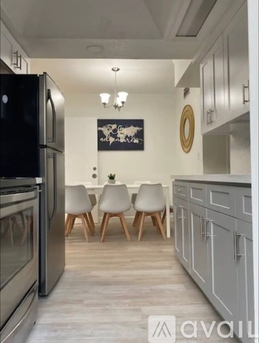 A kitchen with a black fridge, wooden chairs and a painting on the wall.
