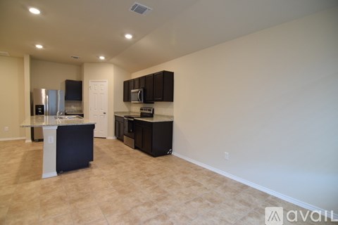 A kitchen area with black cabinets and appliances in a room with beige flooring and walls.