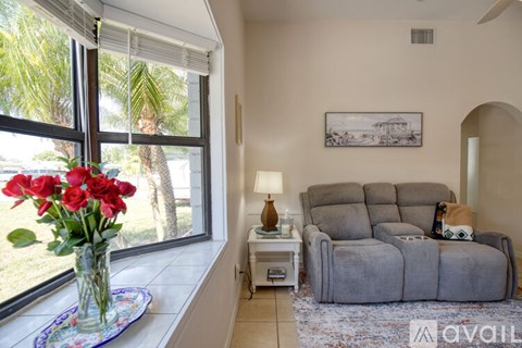 A living room with a grey couch, a vase of red roses, and a painting on the wall.