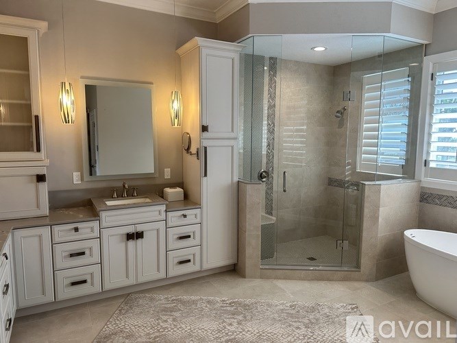 A bathroom with a white cabinet, sink, and shower.