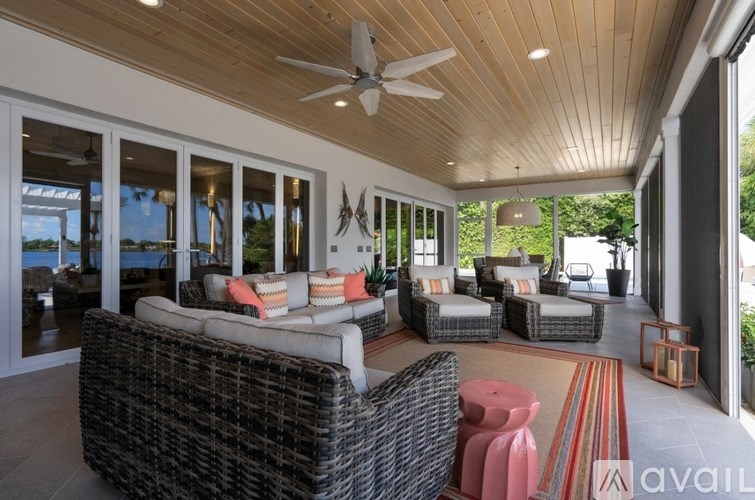 A patio with a black wicker couch and a ceiling fan.