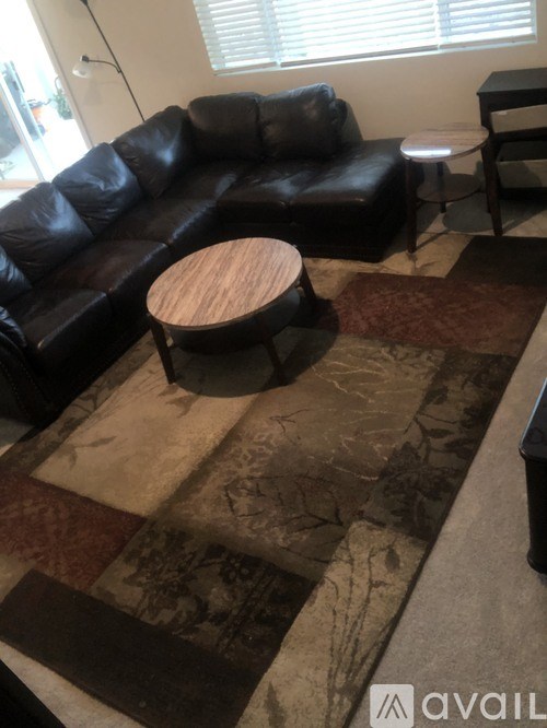 A black leather couch with a wooden stool in front of it.