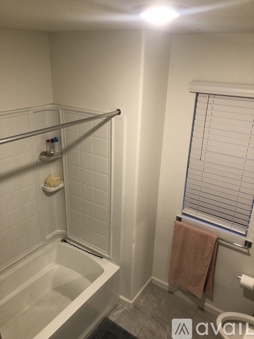 A bathroom with a white tub and a window with blinds.