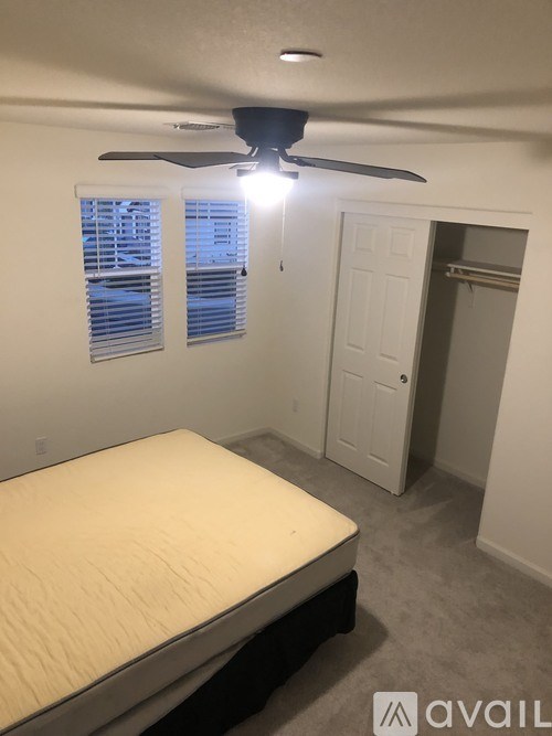 A bedroom with a bed, ceiling fan, and a window with blinds.