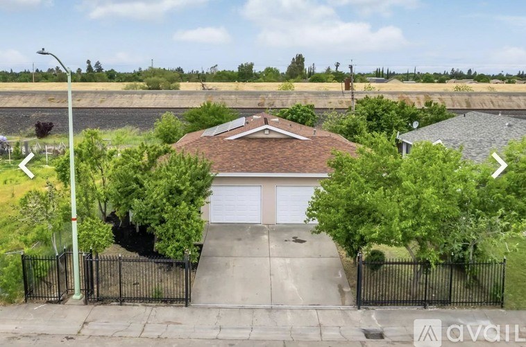 A house with a garage is surrounded by a black fence and has trees on either side.
