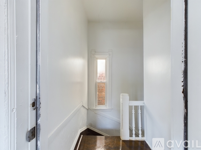 A hallway with white walls and a wooden floor leading to a door.
