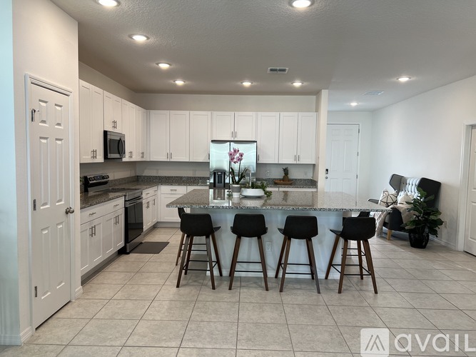 A kitchen with white cabinets and a large island with four black stools.