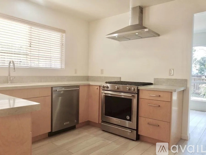 A kitchen with a stainless steel dishwasher and oven, wooden cabinets, and a marble countertop.