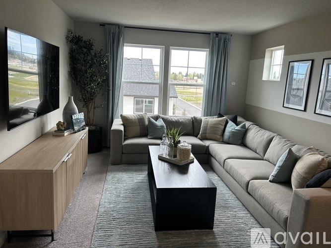 A living room with a grey couch, a wooden cabinet, and a large window with a view of the outside.
