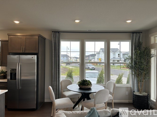 A kitchen with a refrigerator, table and chairs with a view of the street outside.