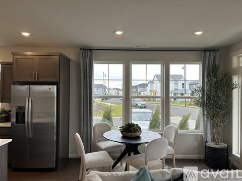 A kitchen with a refrigerator, table and chairs with a view of the street outside.