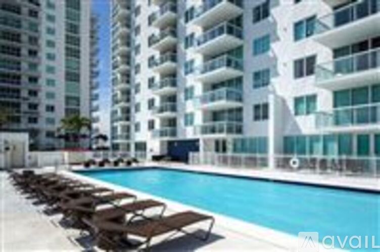 A pool surrounded by lounge chairs in front of a white building.
