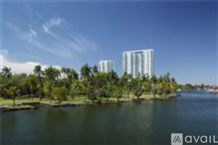 Two tall buildings are situated on a small island with trees.