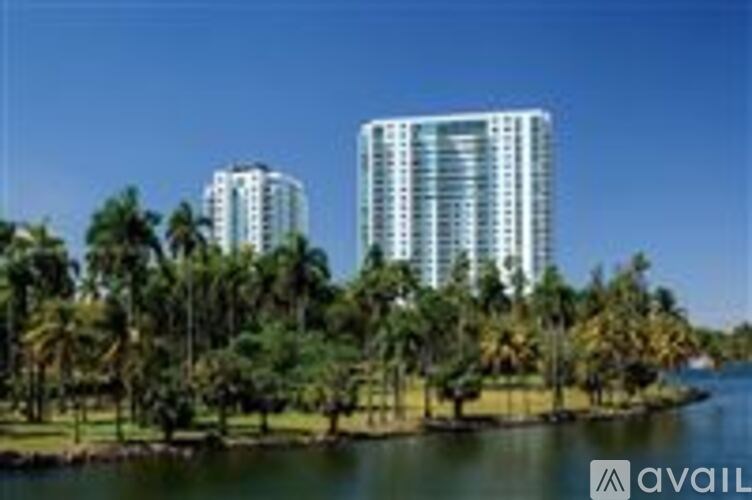 Two high-rise buildings are surrounded by palm trees and water.