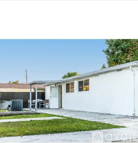 A white house with a patio and a tree in the background.