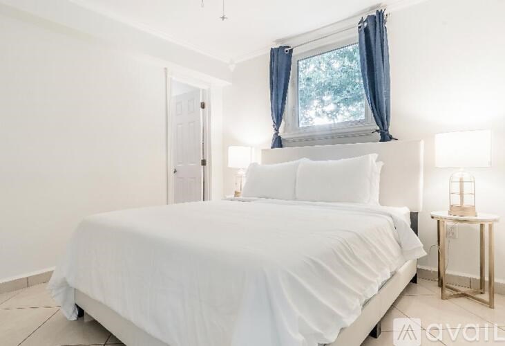 A white bed with a white bedspread and two white pillows is in a room with a window and a door.