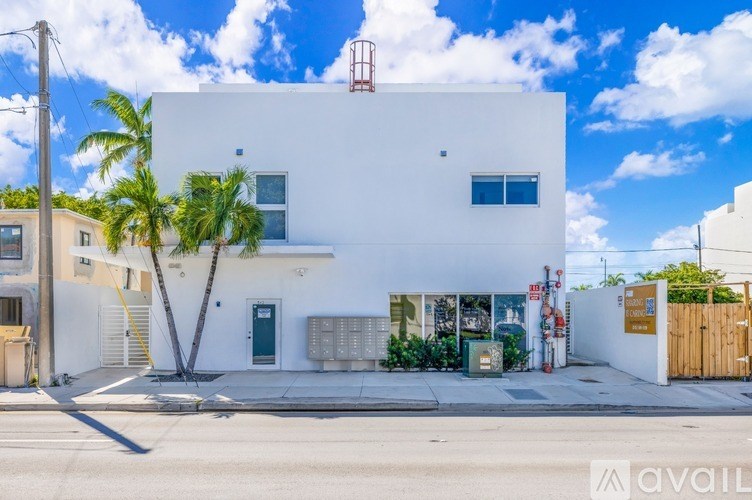 A white building with a blue door and windows is surrounded by palm trees.