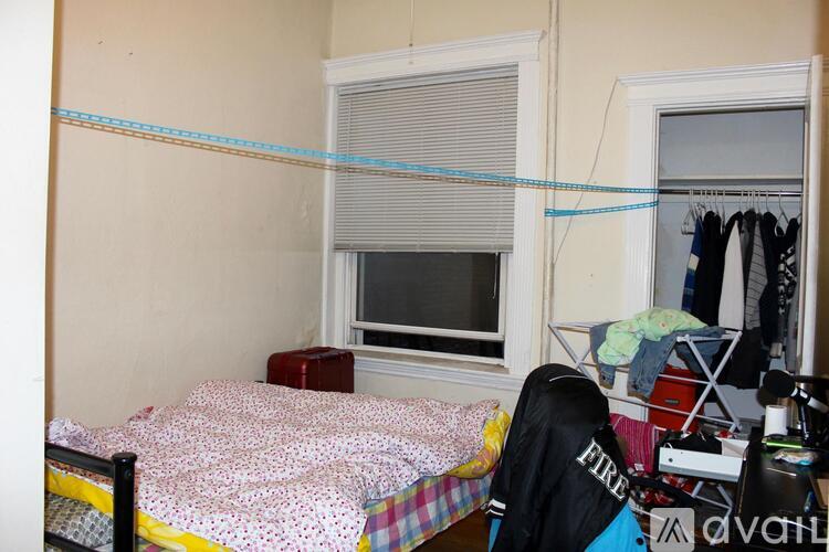 A bedroom with a bed, a window with blinds, and a clothing rack.