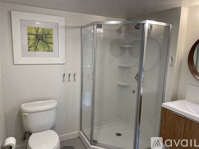 A bathroom with a toilet, a shower with a glass door, and a picture on the wall.
