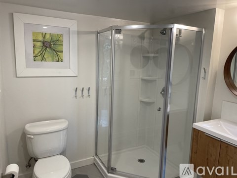 A bathroom with a toilet, a shower with a glass door, and a picture on the wall.