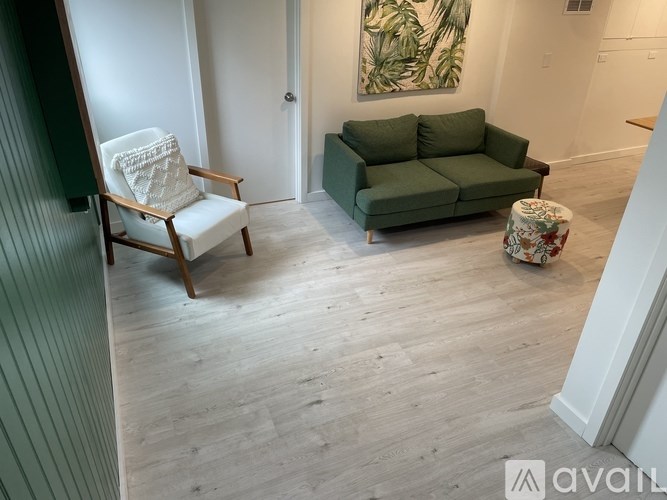 A room with a green couch, a wooden chair, and a floral ottoman.