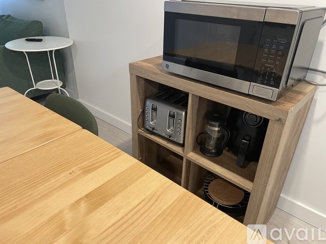 A microwave is on top of a wooden stand with a table in front of it.
