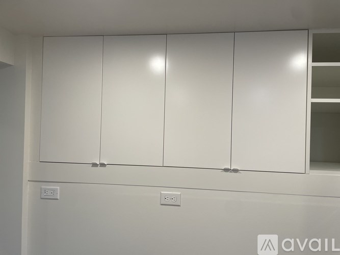 A white cabinet with three doors and a shelf is mounted on a wall.