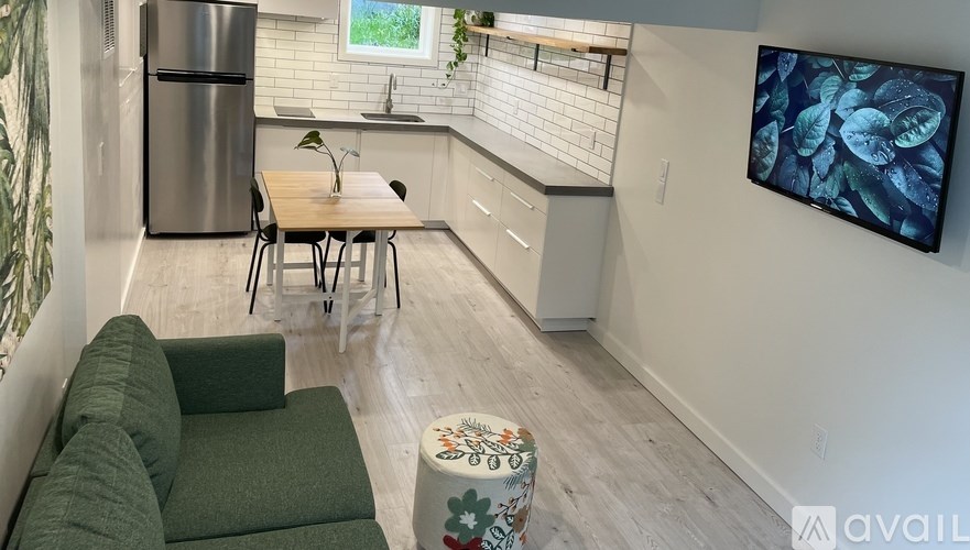 A modern kitchen with a dining table and chairs, a refrigerator, and a television mounted on the wall.