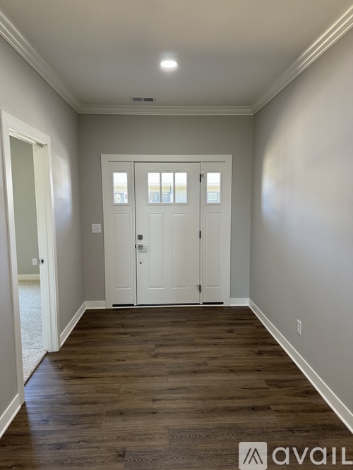 A hallway with wood floors and white walls leading to a set of double doors.