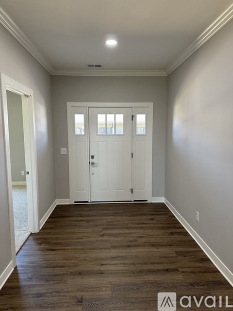 A hallway with wood floors and white walls leading to a set of double doors.
