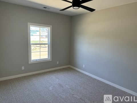 A room with a carpeted floor, a ceiling fan, and a window.