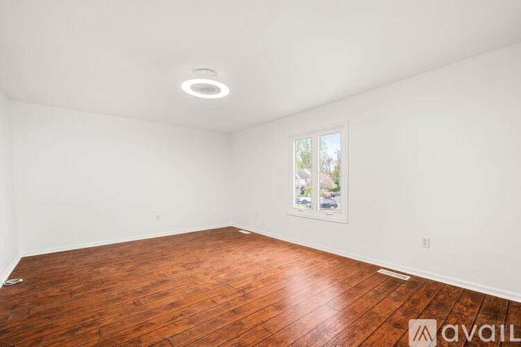 A room with wooden flooring and a window showing trees outside.