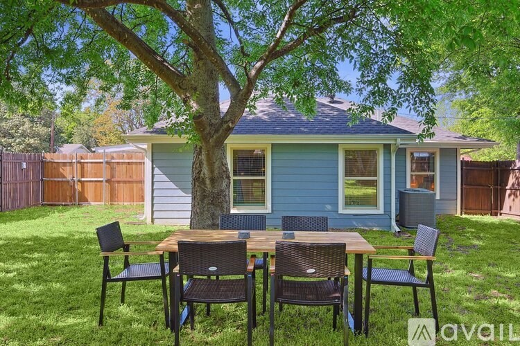 A blue house with a tree in front and a table and chairs in the yard.