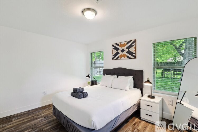 A bedroom with a large bed, a window with a view of a tree, and a wall hanging.