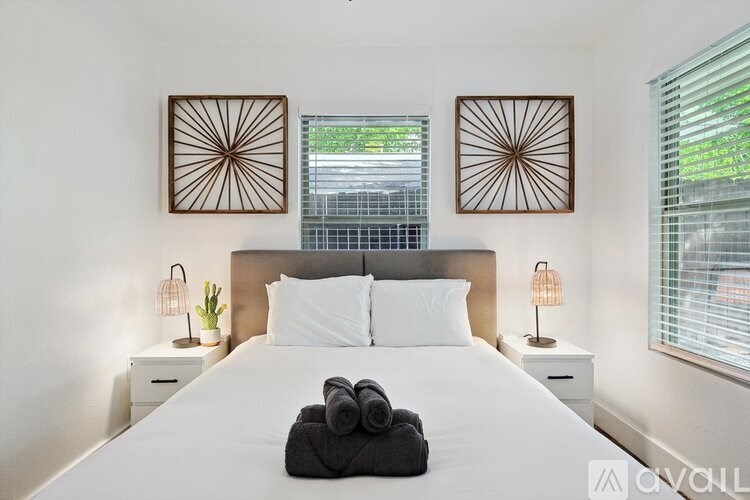 A bedroom with a white bed, two lamps, and two wall art pieces.