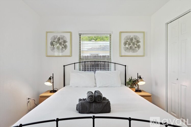 A bedroom with a white bed and two framed artworks on the wall.