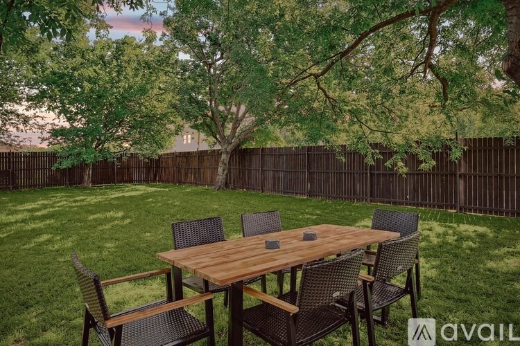 A wooden table with chairs is set up in a grassy backyard.