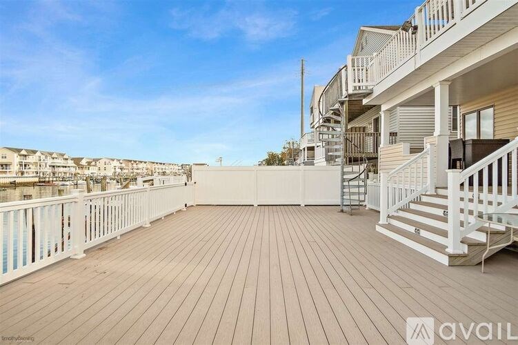 A wooden deck with stairs and railings leading to a balcony overlooking a residential area.