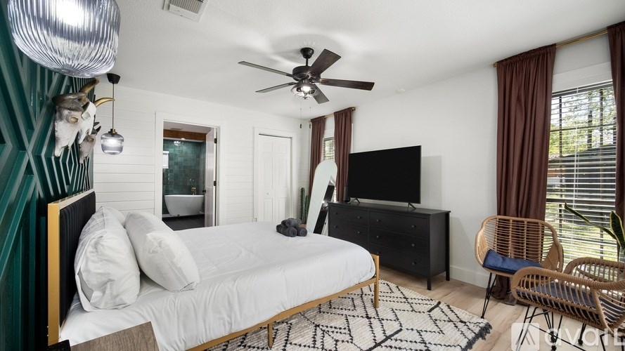 A bedroom with a bed, a TV, a chair, and a ceiling fan.