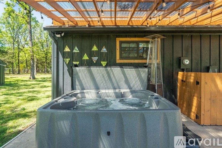 A hot tub sits on a patio under a wooden roof with a fan and a window.