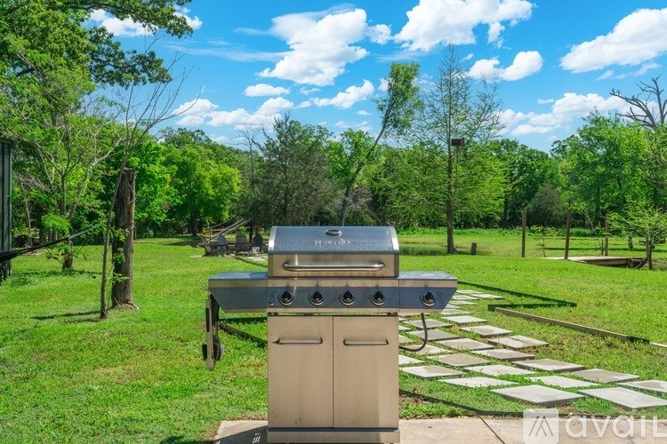 A silver outdoor grill is in the middle of a grassy area with trees in the background.